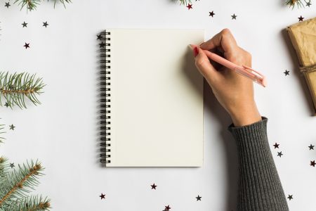 Goals plans dreams make to do list for new year christmas concept writing in notebook. Woman hand holding pen on notebook with fir branches gift on white background. New year winter holiday xmas